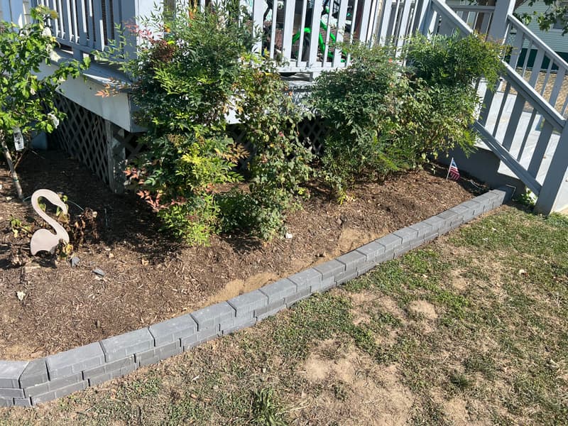Gray paver-block edging around a garden bed under deck stairs